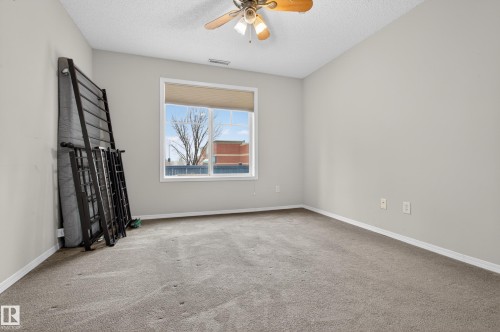 This room features light grey walls, grey carpeting, a window with a roller shade, and a ceiling fan - 131 2098 Blackmud Creek Drive Sw, Edmonton, AB - Indoor Photo Showing Other Room
