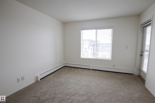 The room features light-colored carpeting, a large window with blinds, and a door with a screen - 405 534 Watt Boulevard, Edmonton, AB - Indoor Photo Showing Other Room