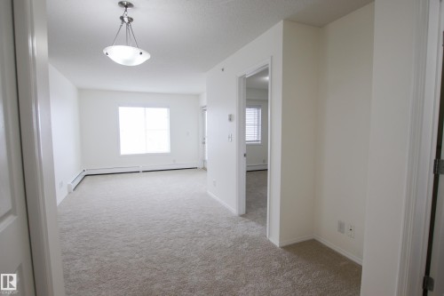 Spacious living area featuring light-colored carpeting, white walls, and a large window providing natural illumination - 405 534 Watt Boulevard, Edmonton, AB - Indoor Photo Showing Other Room