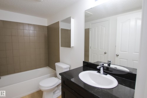 Bathroom featuring a white bathtub, tiled shower surround, toilet, and vanity with a sink and mirror - 405 534 Watt Boulevard, Edmonton, AB - Indoor Photo Showing Bathroom