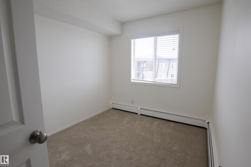 This room features a window with blinds, light-colored walls, and carpeted flooring - 405 534 Watt Boulevard, Edmonton, AB - Indoor Photo Showing Other Room