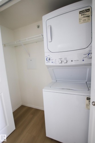 Dedicated laundry area featuring a stackable washer and dryer, a wire shelf, and wood-look flooring - 405 534 Watt Boulevard, Edmonton, AB - Indoor Photo Showing Laundry Room