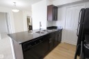 The kitchen features dark wood cabinetry, a double basin stainless steel sink, black countertops, and light wood flooring - 405 534 Watt Boulevard, Edmonton, AB  - Indoor Photo Showing Kitchen With Double Sink 