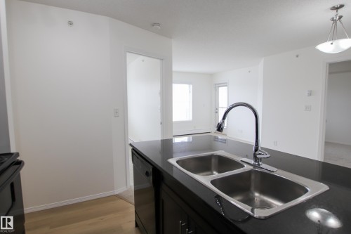 Kitchen island featuring a double basin stainless steel sink with a high-arc faucet, set within a dark countertop - 405 534 Watt Boulevard, Edmonton, AB - Indoor Photo Showing Kitchen With Double Sink