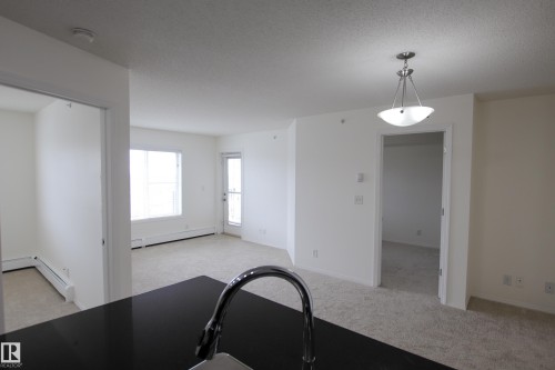 The property features a spacious room with carpeted flooring, a window providing natural light, and a door leading to an exterior space - 405 534 Watt Boulevard, Edmonton, AB - Indoor Photo Showing Other Room