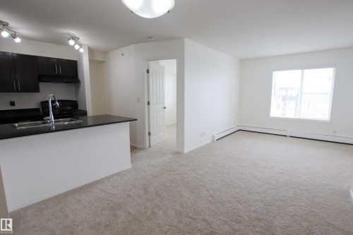 This open-concept living area features light-colored carpeting, white walls, and a large window - 405 534 Watt Boulevard, Edmonton, AB - Indoor