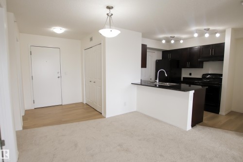 Open concept living space featuring a kitchen with dark cabinetry, black appliances, and a breakfast bar with a sink and a chrome faucet - 405 534 Watt Boulevard, Edmonton, AB - Indoor Photo Showing Kitchen