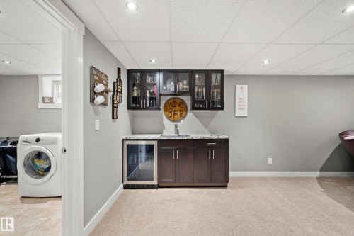 Recreation room featuring a wet bar with dark cabinetry, granite-style countertops, and glass-front upper cabinets - 635 41 Avenue, Edmonton, AB - Indoor