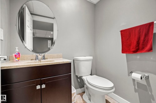Well-appointed bathroom featuring a vanity with a light-colored countertop and a dark wood cabinet, a wall-mounted oval mirror, and a toilet - 635 41 Avenue, Edmonton, AB - Indoor Photo Showing Bathroom