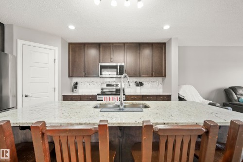 The kitchen features a spacious island with a light-colored countertop, dark wood cabinetry, a stainless steel sink with a high-arc faucet, and stainless steel appliances - 635 41 Avenue, Edmonton, AB - Indoor Photo Showing Kitchen With Double Sink