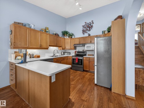 The kitchen features wooden cabinetry, white countertops, a stainless steel refrigerator, and hardwood flooring - 7 85 Gervais Road, St. Albert, AB - Indoor Photo Showing Kitchen With Double Sink