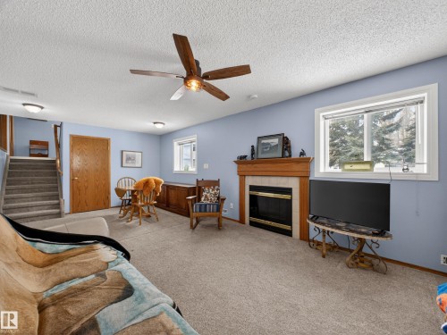 Living area featuring carpeted flooring, a fireplace with a wooden mantel and light-colored tile surround, and a ceiling fan - 7 85 Gervais Road, St. Albert, AB - Indoor With Fireplace