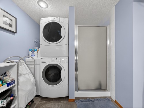 This space features a stacked washer and dryer, an enclosed shower, and a built-in shelf for storage - 7 85 Gervais Road, St. Albert, AB - Indoor Photo Showing Laundry Room