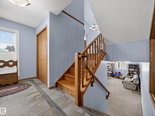 Entranceway featuring tile flooring, a window providing natural light, and a wooden staircase with a railing - 7 85 Gervais Road, St. Albert, AB - Indoor Photo Showing Other Room
