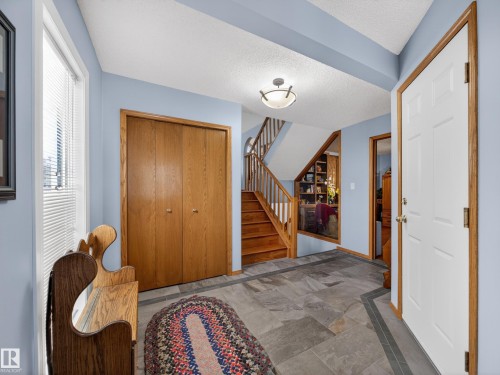 The welcoming entryway features slate flooring, a wooden staircase, and a wood-paneled closet - 7 85 Gervais Road, St. Albert, AB - Indoor Photo Showing Other Room