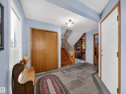 The welcoming entryway features slate flooring, a wooden staircase, and a wood-paneled closet - 