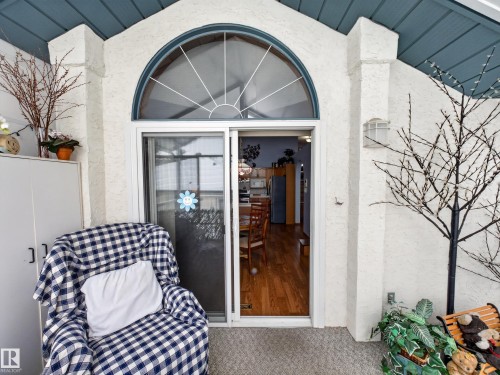 The property features an exterior patio with a textured wall, a sliding glass door with an arched transom window, and a ceiling with exposed beams - 7 85 Gervais Road, St. Albert, AB - Outdoor
