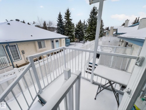 The property features a private balcony with white railings, offering views of surrounding residential structures and mature evergreen trees - 7 85 Gervais Road, St. Albert, AB - Outdoor With Exterior