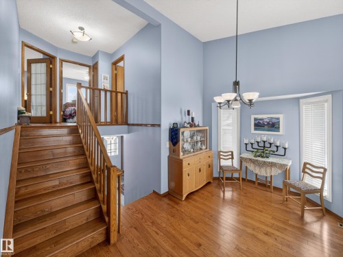 This property features a grand staircase with hardwood treads and a matching wooden railing, complemented by hardwood flooring throughout the main level - 7 85 Gervais Road, St. Albert, AB - Indoor Photo Showing Other Room