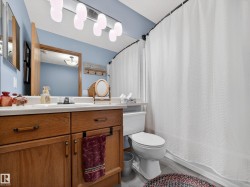The bathroom features a light blue wall, a vanity with a white countertop and oak-toned cabinetry, and a white toilet - 
