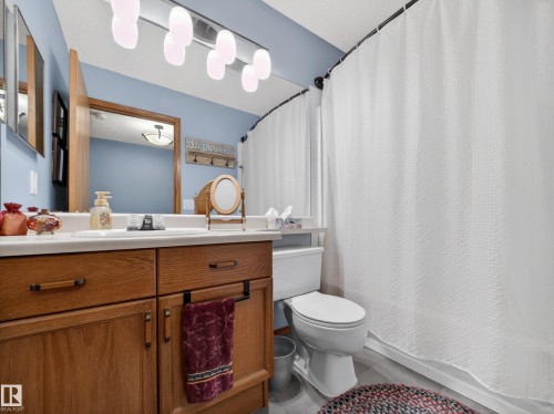 The bathroom features a light blue wall, a vanity with a white countertop and oak-toned cabinetry, and a white toilet - 7 85 Gervais Road, St. Albert, AB - Indoor Photo Showing Bathroom