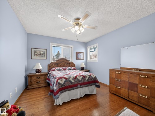 Bedroom featuring hardwood floors, two windows providing natural light, a ceiling fan with integrated lighting, and light blue walls - 7 85 Gervais Road, St. Albert, AB - Indoor Photo Showing Bedroom