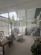 Enclosed sunroom featuring a pitched ceiling, full-height windows, a glass-paneled entry door, and light-toned carpeting - 