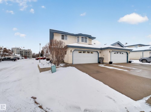 The property features a two-story exterior with light-colored siding and a blue roof trim, complemented by attached garages with white doors - 7 85 Gervais Road, St. Albert, AB - Outdoor