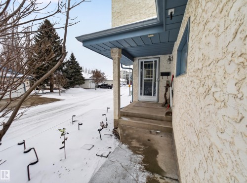 The property features a front entrance with a screen door, a textured exterior, and a covered porch - 7 85 Gervais Road, St. Albert, AB - Outdoor