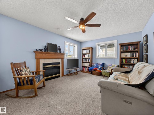 The living space features a fireplace with a wooden mantel, light blue walls, and a ceiling fan - 7 85 Gervais Road, St. Albert, AB - Indoor Photo Showing Living Room With Fireplace