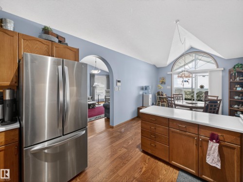 The kitchen features a stainless steel refrigerator, wooden cabinetry, and a central island with a white countertop - 7 85 Gervais Road, St. Albert, AB - Indoor Photo Showing Kitchen