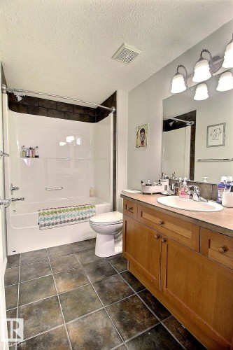 The bathroom features a vanity with a counter and an integrated sink, a mirror with overhead lighting, and a shower-tub combination with dark tile surround - 114 592 Hooke Road, Edmonton, AB - Indoor Photo Showing Bathroom