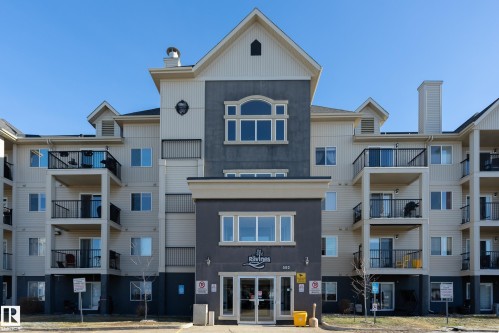 The property features a multi-story building with balconies, a prominent main entrance, and a light-colored exterior with darker accents - 114 592 Hooke Road, Edmonton, AB - Outdoor With Facade