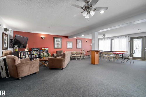 This spacious common area features carpeted flooring, a ceiling fan, and large windows with white curtains providing natural light - 114 592 Hooke Road, Edmonton, AB - Indoor