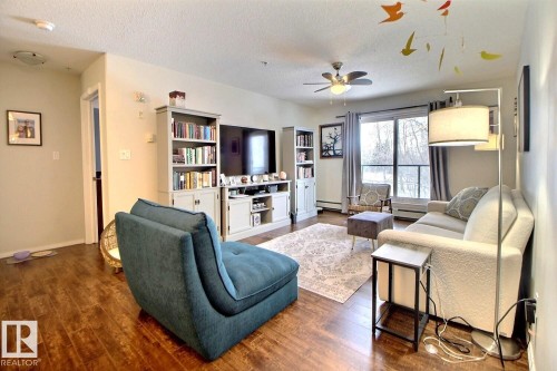 The living area features wood flooring, a ceiling fan, and large windows providing natural light - 114 592 Hooke Road, Edmonton, AB - Indoor Photo Showing Living Room