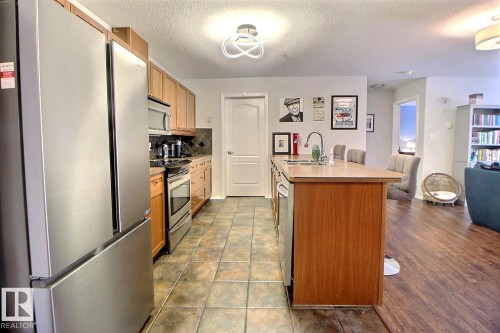 The kitchen features stainless steel appliances, wood cabinetry, and a central island with a sink - 114 592 Hooke Road, Edmonton, AB - Indoor Photo Showing Kitchen