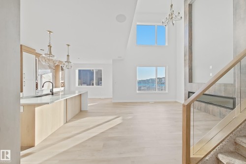 The open concept interior features light-toned hardwood flooring, a contemporary kitchen island with a dark faucet, and a fireplace with a dark rectangular insert - 6449 28 Avenue, Edmonton, AB - Indoor Photo Showing Other Room