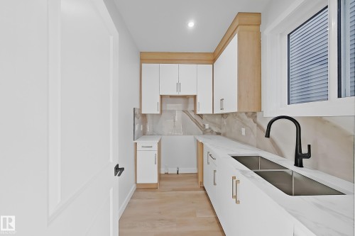 Kitchenette featuring white cabinetry with gold-toned hardware, light wood accents, a double sink with a matte black faucet, and a large window providing natural light - 6449 28 Avenue, Edmonton, AB - Indoor Photo Showing Kitchen With Double Sink