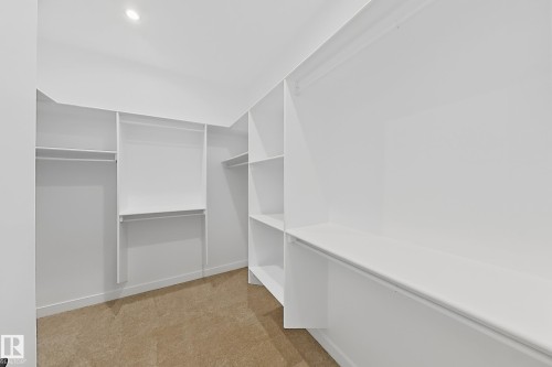 This walk-in closet features extensive built-in shelving, hanging rods, and recessed lighting, all set against a neutral-toned carpet - 6449 28 Avenue, Edmonton, AB - Indoor With Storage