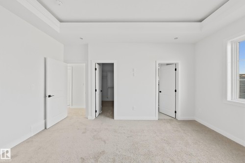 This spacious room features a tray ceiling, light-colored carpet, and white walls, creating a bright and open atmosphere - 6449 28 Avenue, Edmonton, AB - Indoor Photo Showing Other Room