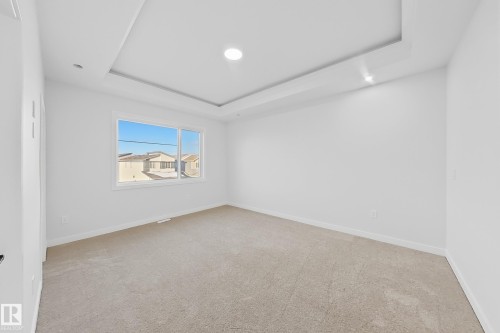 This room features a tray ceiling with recessed lighting, light-colored carpet, and a window providing natural light and views of other properties - 6449 28 Avenue, Edmonton, AB - Indoor Photo Showing Other Room