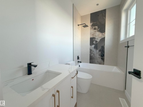 The bathroom features a modern vanity with a white countertop and gold-toned hardware, a sleek black faucet, and a contemporary bathtub with a black shower head - 6449 28 Avenue, Edmonton, AB - Indoor Photo Showing Bathroom