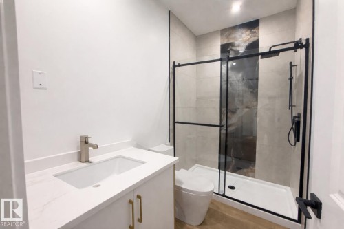 Contemporary bathroom featuring a vanity with a white countertop and gold-toned hardware, a walk-in shower with a black-framed glass enclosure, and modern fixtures - 6449 28 Avenue, Edmonton, AB - Indoor Photo Showing Bathroom