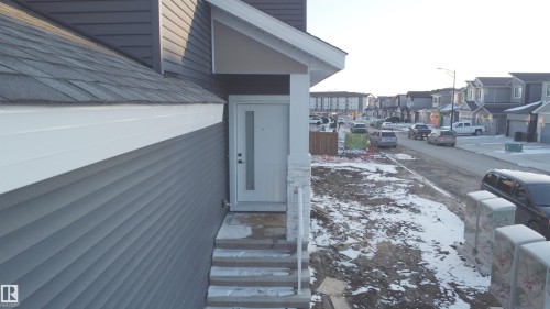 The property features a white front door with a frosted glass insert, gray siding, and a gabled roof with dark shingles - 6449 28 Avenue, Edmonton, AB - Outdoor