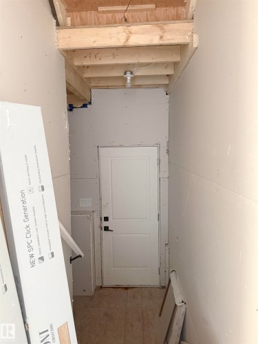 The property features a white paneled door with black hardware, surrounded by unfinished drywall, and exposed wooden ceiling joists - 6449 28 Avenue, Edmonton, AB - Indoor Photo Showing Other Room