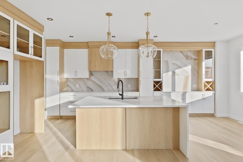 Contemporary kitchen featuring light wood flooring, white cabinetry, and a central island with a sink and a black faucet - 6449 28 Avenue, Edmonton, AB - Indoor Photo Showing Kitchen