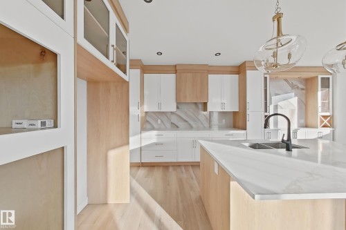 The kitchen features a large island with a sink and a dark-toned faucet, light wood flooring, and a mix of white and light wood cabinetry - 6449 28 Avenue, Edmonton, AB - Indoor Photo Showing Kitchen With Double Sink