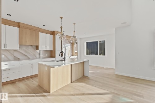 The kitchen features a center island with a sink, white cabinetry, light wood-toned upper cabinets, and a white marble-patterned backsplash - 6449 28 Avenue, Edmonton, AB - Indoor Photo Showing Kitchen