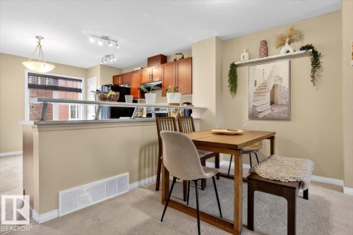The property features an open-concept living area with carpeting, a kitchen with rich wood cabinetry and track lighting, and a dining area - 1637 Towne Centre Boulevard, Edmonton, AB - Indoor Photo Showing Dining Room