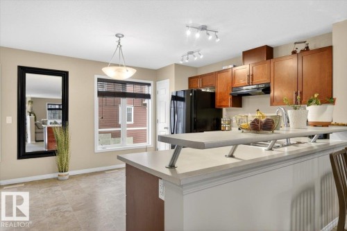 The kitchen features wood cabinetry, a breakfast bar with a light-colored countertop, and a black refrigerator - 1637 Towne Centre Boulevard, Edmonton, AB - Indoor Photo Showing Kitchen